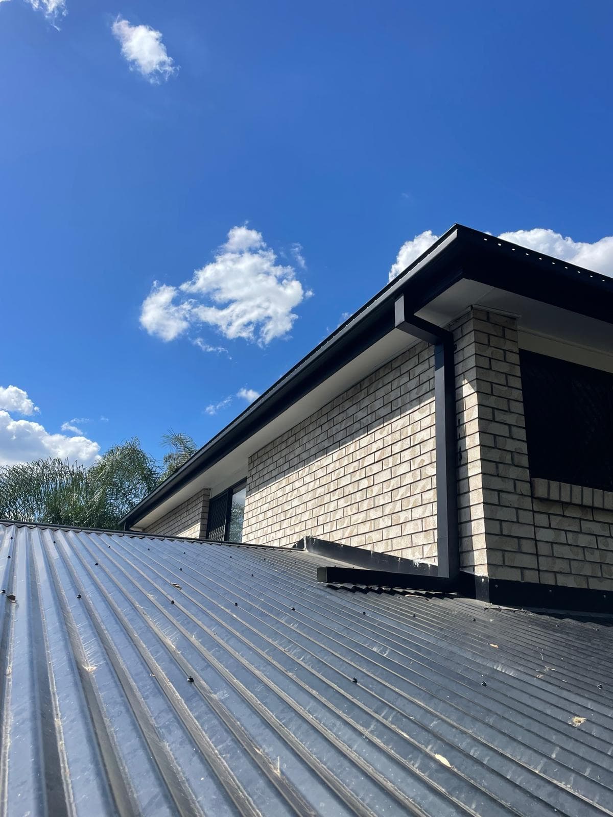 Black gutters and fascia against cream brick under a clear sky